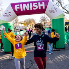 Girls on the Run participant has her arms in the air as she completes the 5K. Her 5K Buddy cheers her on.